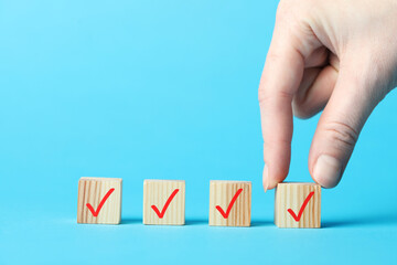 Woman taking wooden cube with check mark on light blue background, closeup