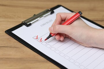 Woman filling Checklist with marker at wooden table, closeup