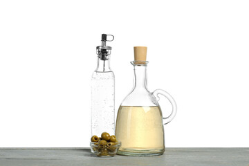 Vinegars in bottles and olives on grey wooden table against white background