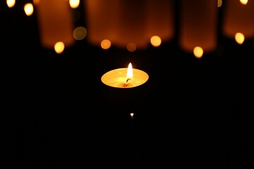 Burning candle on dark surface, closeup. Bokeh effect