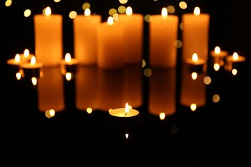 Burning candles on mirror surface in darkness. Bokeh effect