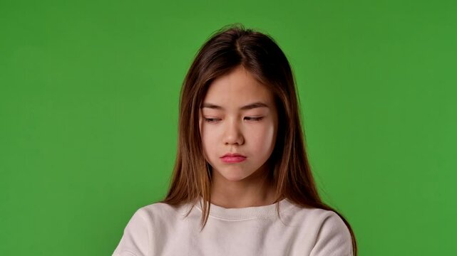 Asian girl child with sad angry face looks at camera, negative expression, isolated on chroma key green screen studio background mockup.