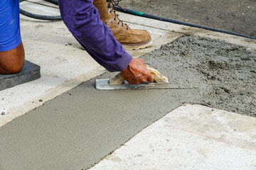 Hands using a trowel to smooth fresh wet concrete