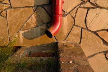 Rain gutter pipe is attached to a stone wall. Metallic guttering system.