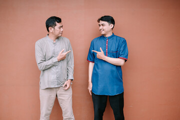 Two smiling men pointing at each other standing in front of a plain wall