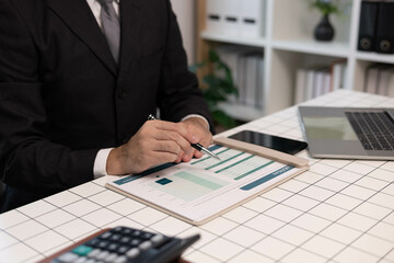 A man in a suit is holding a pen and looking at a piece of paper. He is focused and attentive, possibly reviewing some important information or making a decision
