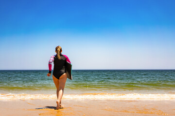 Water sports. Mature woman holding bodyboard running out of water on sunny beach. Back view