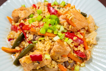On a wooden table in a plate there are vegetables stewed with bulgur and meat