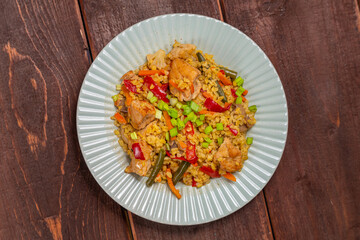 On a wooden table in a plate there are vegetables stewed with bulgur and meat