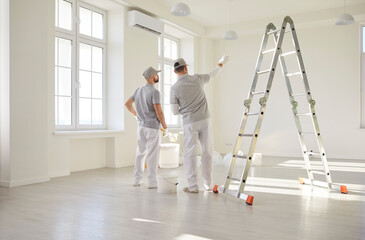 Two professional painters or building contractors in light clothes standing back and discussing...