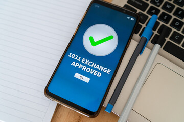 1031 Exchange approval notification on smartphone. Concept of like-kind property transaction under...