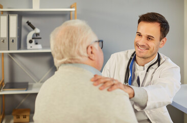 Friendly smiling male doctor comforting patient during consultation in medical office. Caring...