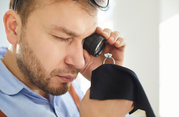 Close up of young professional male jeweler or jewellery appraiser examining gold ring with large...