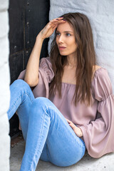 Portrait of a young beautiful brunette girl in blue jeans posing in a stone arch