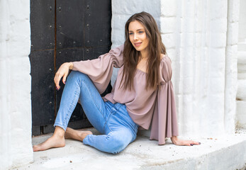 Portrait of a young beautiful brunette girl in blue jeans posing in a stone arch