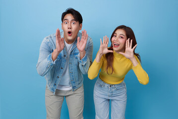 Young lovely asian couple yelling announce with hands cup around mouths isolated on blue studio...