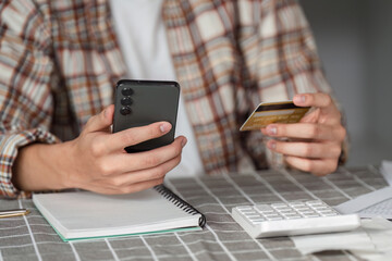 Teenager using smartphone and credit card for online shopping, enjoying the process.