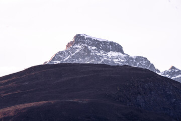 mountain peak snow cap partially illuminated at sunset. detail of cliff. soft rose colored cloudy sky. close up