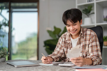 Teenager managing finances at home, reviewing bills and budgeting with a smile.