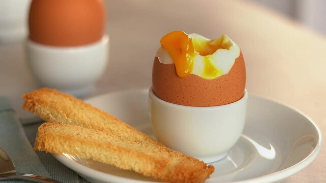 Close up of fresh crispy bread crouton dips in soft-boiled egg in egg cup. Chicken yolk flows down egg. Breakfast concept. Food background