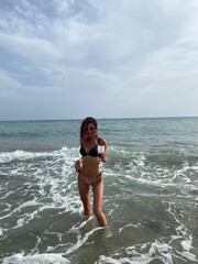 Young woman enjoying a refreshing drink while relaxing in the ocean waves on a sunny beach day