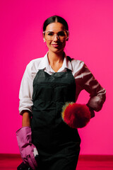 Expert female cleaner poses confidently against a vibrant pink background showcasing her cleaning...