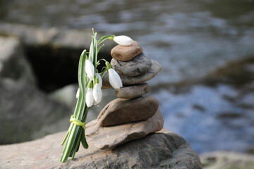 Meditation am Fluss mit Balancepyramide und Blumenstrauss mit Schneeglöckchen auf Felsen 