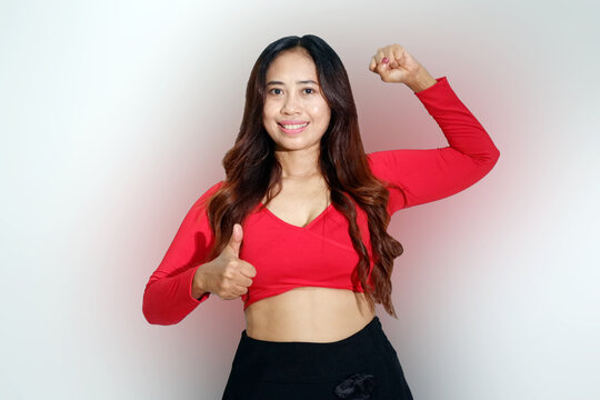 Smiling Asian fitness girl showing muscles on arm, flexing biceps and looking happy at camera, wearing sportswear and giving thump up isolated on white background