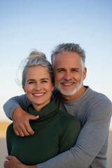 Obraz premium A couple is posing for a picture with a blue sky in the background. The man is wearing a gray shirt and the woman is wearing a green sweater. They both have smiles on their faces