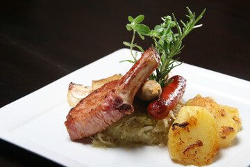 Succulent smoked pork chop beside grilled sausages, tangy sauerkraut, crispy roasted potatoes, garnished with fresh rosemary