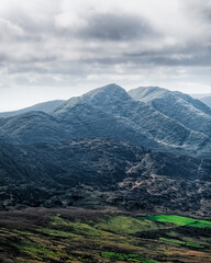 The Carrauntoohil walkway in Ireland, taking in the breathtaking landscape of rugged hills and vibrant green fields under a dynamic sky filled with clouds.