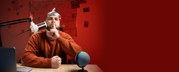 Bearded man in aluminum foil hat press finger to lips, shush shh gesture while sitting in the...