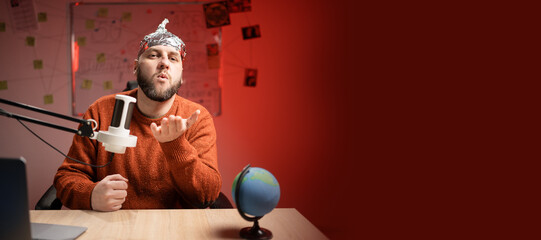 Bearded man in aluminum foil hat sending air kiss while Live streaming, presenter with microphone...