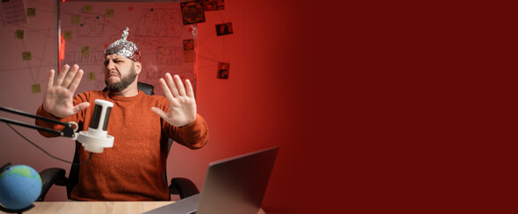 Bearded man in aluminum foil hat Moving away hands palms showing refusal while Live streaming,...