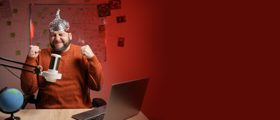 Bearded man in aluminum foil hat showing stress gesture with fists while Live streaming, presenter...