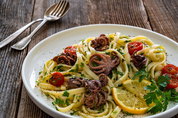 Pasta with baby octopus on wooden table	