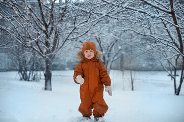 Winter. New Year and Christmas holidays. A child walks in the snow in a warm winter jumpsuit.