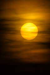 A radiant golden sun shines through soft clouds during a captivating sunset or sunrise.