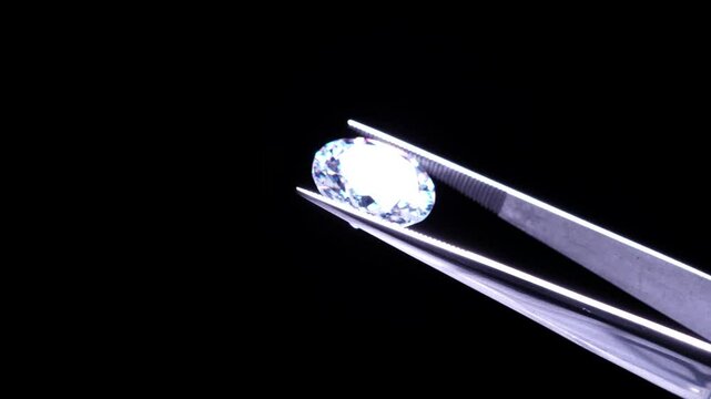Hand held in tweezers diamond quality Inspection, selective focus. Chips and damage look up. Macro close up of luxury brilliant. View under magnifying glass. Round cut stone jewellery. Engagement day