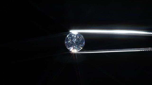 Hand held in tweezers diamond quality Inspection, selective focus. Chips and damage look up. Macro close up of luxury brilliant. View under magnifying glass. Round cut stone jewellery. Engagement day