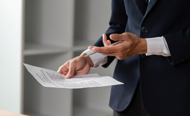 Lawyer standing and reviewing contract documents with pen in hand in modern office.