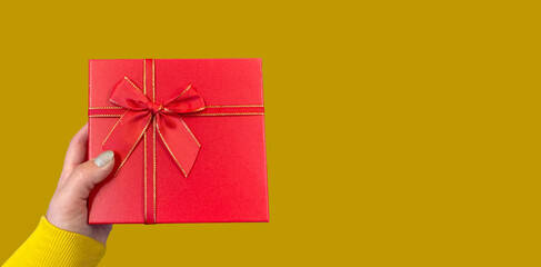 hand holding red gift box with red ribbon on yellow background