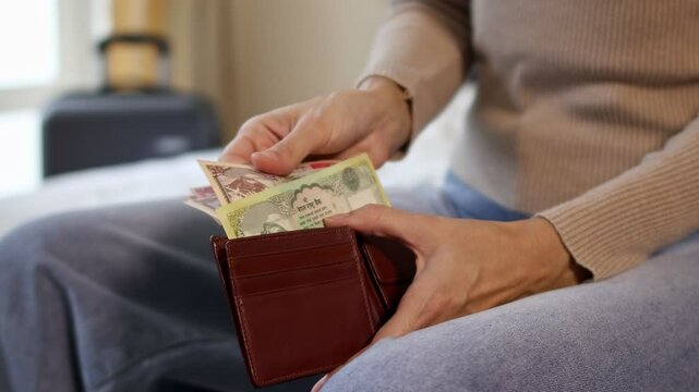 Close up view of a female traveler hands counting Nepalese rupee cash money while packing a suitcase for a holiday trip. Preparing money and luggage for vacation. Concept of travel expenses in Nepal.