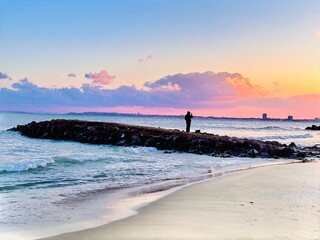 a man watches the sunset standing on the breakwater on the beach