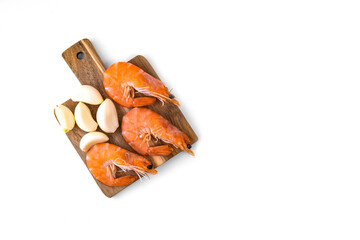 boiled shrimp with a bright orange shell and cloves of garlic on a wooden board on a white background