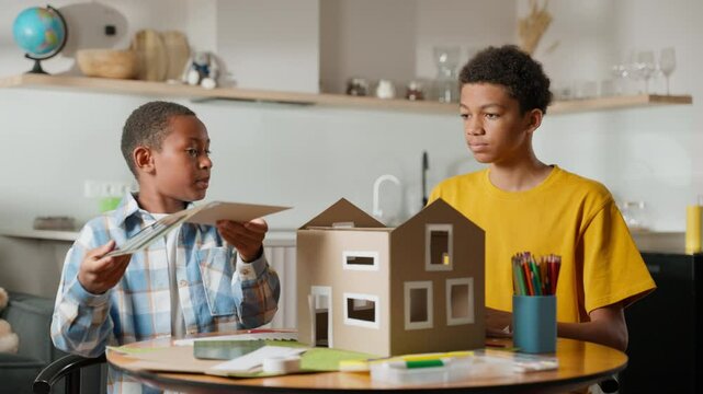 Both brothers work together to attach roof with solar panels to model house. This moment captures their cooperative effort, show problem-solving and teamwork in key parts of school science project