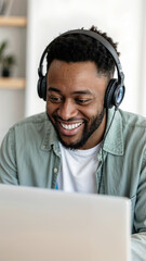 A smiley young African American man in front of laptop monitor in headphones during online video call.
