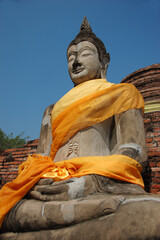 Row of sacred Buddha statues in Ayutthaya, Thailand, draped with orange scarves, symbolizing...