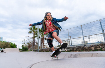 Beautiful active senior woman skateboarding at skate city park - Mature adult female skateboarder...