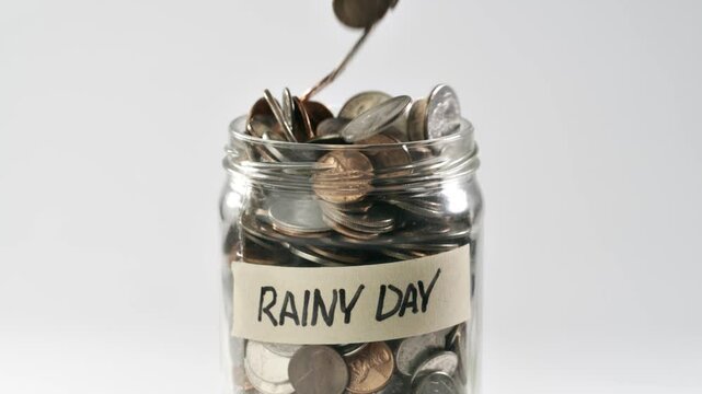 Close-up shot of coins falling in slow motion into a coin jar labled 'Rainy Day'.